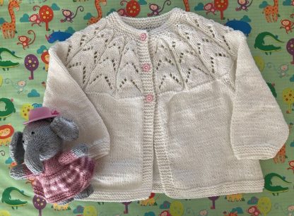 Hand knitted round neck matinee jacket in white with a beautiful lacy yoke 3 pink daisy buttons in front