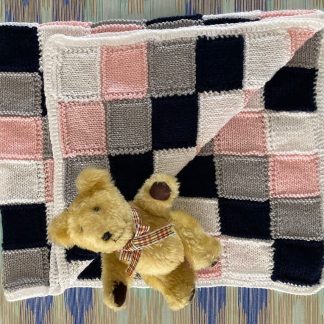 Hand knitted baby’s blanket in pink, white, grey and black in an unusual block pattern