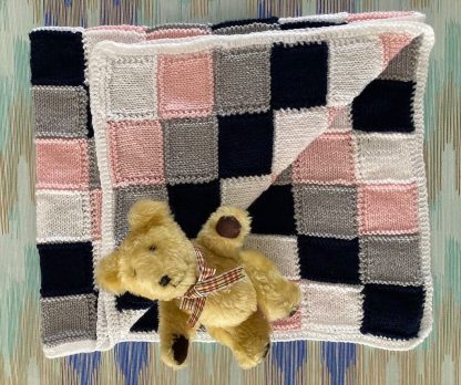 Hand knitted baby’s blanket in pink, white, grey and black in an unusual block pattern