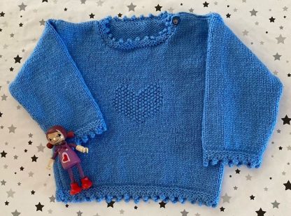 Hand knitted blue jumper with a heart motif Round neck Cute button on one shoulder Long sleeves Picot edging around neckline, cuffs and hem 100% Acrylic yarn