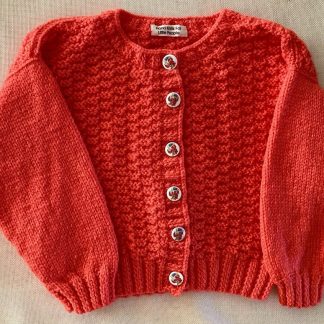 Hand knitted salmon coloured patterned cardigan Round neck 6 Delightful buttons in front Long sleeves Ribbing around neckline, cuffs and hem 100% Acrylic yarn