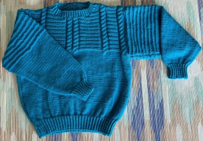 Hand knitted blue jumper in a stunning pattern Round neck Long sleeves Ribbing around neckline, cuffs and hem 100% Acrylic yarn Completed garment measurements Chest all around: 76cm Length, shoulder to hem ribbing: 39cm Sleeve seam length: 35cm For ages 5-6 years