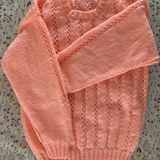 Hand knitted jumper in peach in a beautiful pattern Round neck 3 Unusual buttons on one shoulder Long sleeves Ribbing around neckline, cuffs and hem 100% Acrylic yarn Completed garment measurements Chest all around: 82cm Length, shoulder to hem ribbing: 48cm Sleeve seam length: 38cm For ages 7-8 years